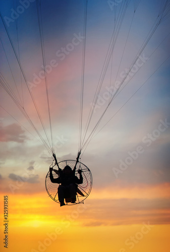 Silhouette Para motor glider flying in the orange sky