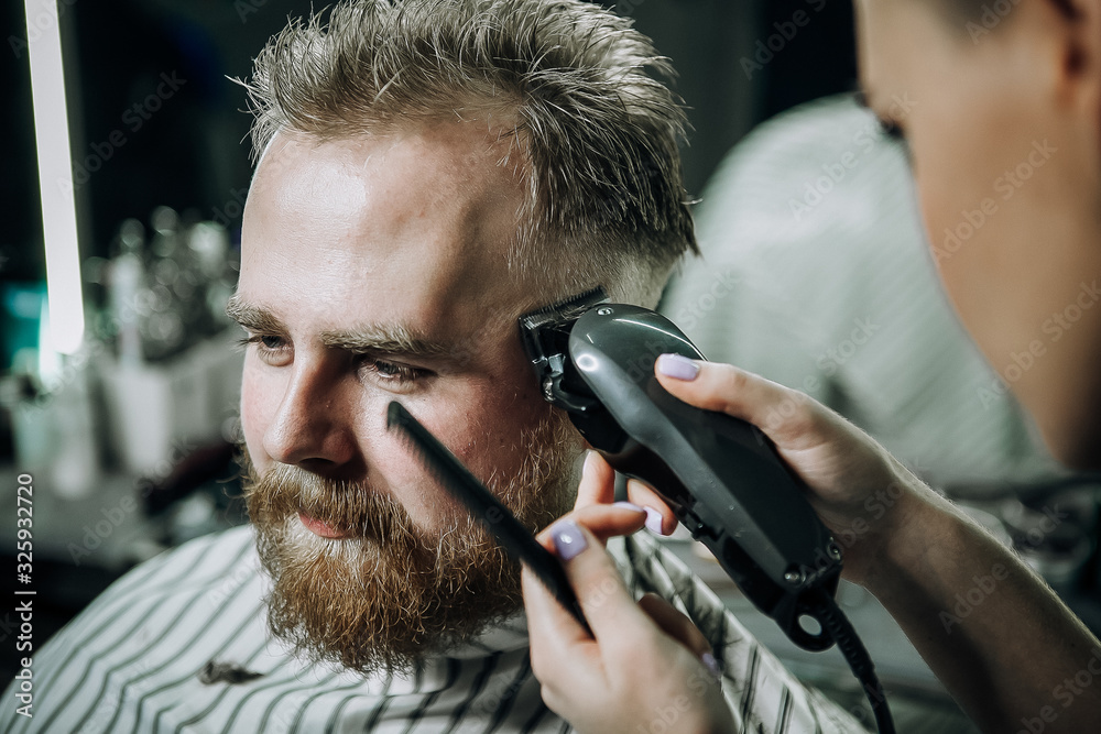 In a barber shop, a young woman cuts a guy with red hair and a red beard In a barber shop, a young woman cuts a guy with red hair and a red beard