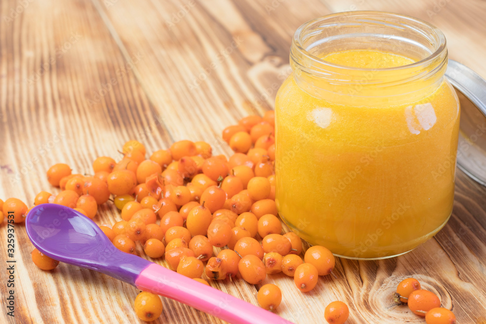 baby sea buckthorn puree in a jar on a wooden table. baby food. baby sea buckthorn puree in a jar on a wooden table. baby food.