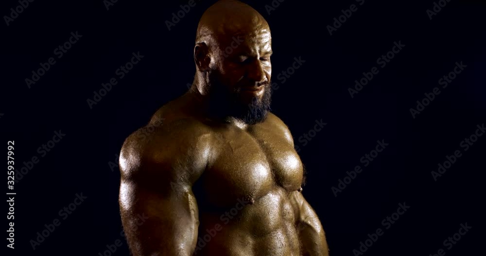 naked bodybuilder man is standing in darkness in studio, showing muscles of torso naked bodybuilder man is standing in darkness in studio, showing muscles of torso