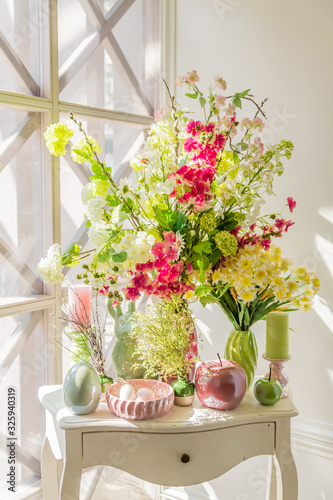 Easter interior decoration. Beautiful composition with candles, eggs, rabbit, apples and blooming flowers on white vintage chestboard..