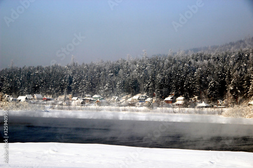 Wallpaper Mural In the background, on the other bank of the river, conifer winter forest begins. Several huts with snow covered roofs near the forest. In the foreground - mist rising from the water and fluffy snow. Torontodigital.ca