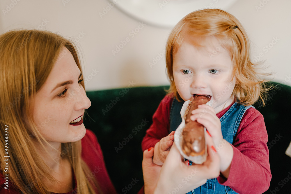 Portrait of happy young mother and daughter child girl are eating tasty cake after dinner, isolated in restaurant. Two sisters eat cupcakes together. Happy loving family. Portrait of happy young mother and daughter child girl are eating tasty cake after dinner, isolated in restaurant. Two sisters eat cupcakes together. Happy loving family.