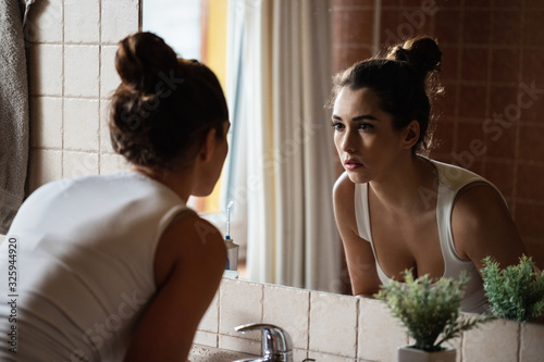 Photography Young woman looking herself in bathroom mirror.