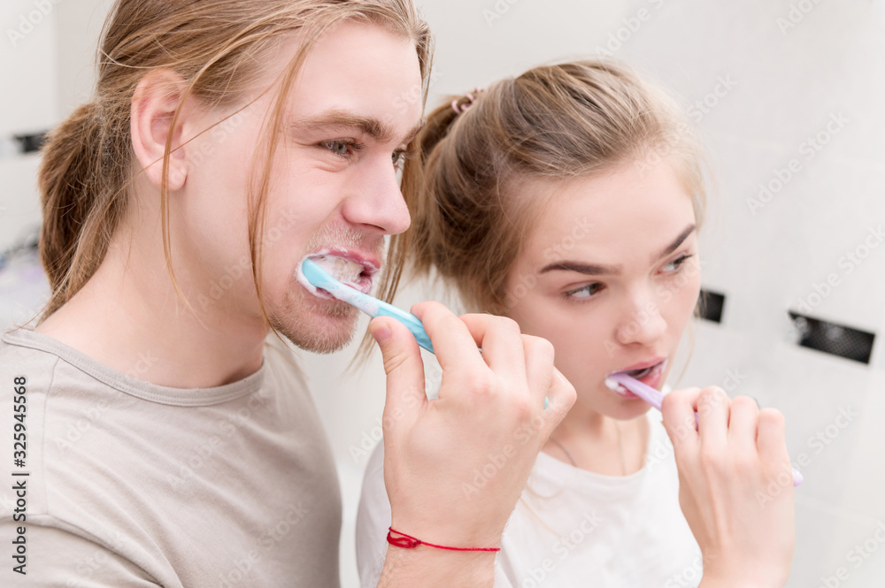 Young couple in bath brush teeth together, looking in mirror. Close-up Young couple in bath brush teeth together, looking in mirror. Close-up