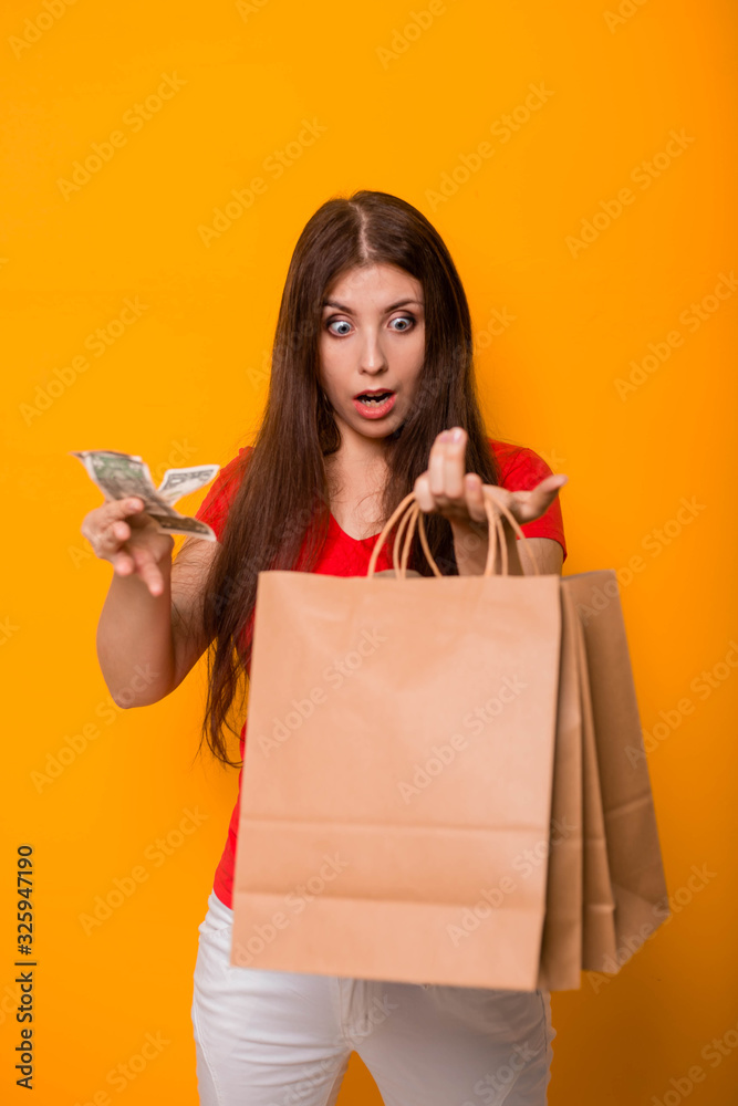 A young, attractive woman with money and packages in her hands, looks at a loss at the remaining money after shopping. A young, attractive woman with money and packages in her hands, looks at a loss at the remaining money after shopping.