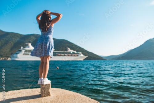 young pretty woman at the edge of the dock with beautiful view of mountains and sea with cruise liner