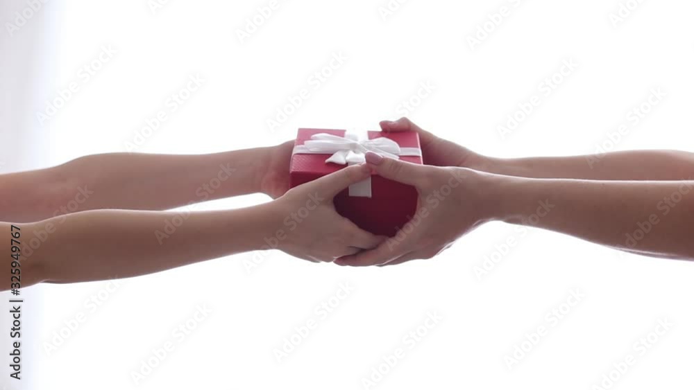 A child gives mom a small gift in a red box with a white bow A child gives mom a small gift in a red box with a white bow