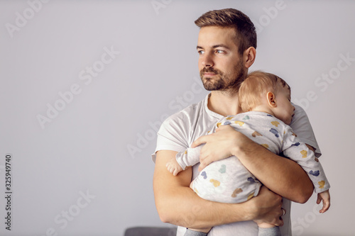 Portrait of handsome father holding his beloved sleeping son and looking away. He is finally succeeded to put him to sleep. photo