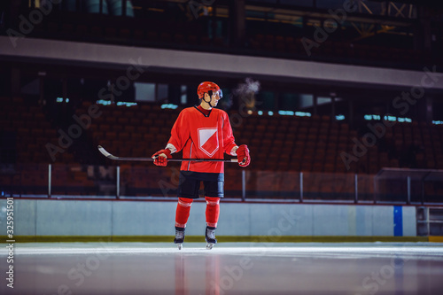 Full length of hockey player standing on ice with stick in his hands and waiting for teammates to pass him a puck.