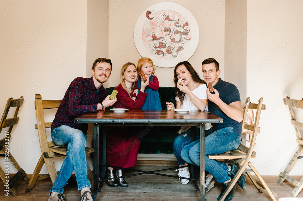 Group of five friends having fun a coffee together. Two women and child and two men at cafe talking laughing and enjoying their time. Celebrate Happy Day 8 March.