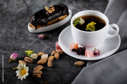 A cup of tea with chocolate eclair and pistachios on a dark table