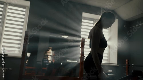 Sporty girl does biceps exercise in the gym. The rays of the sun shine brightly through the window