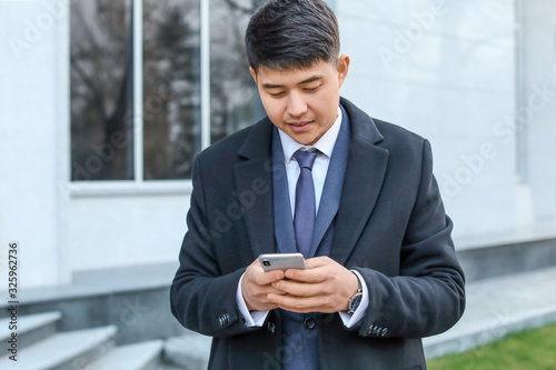 Young Asian businessman with mobile phone outdoors