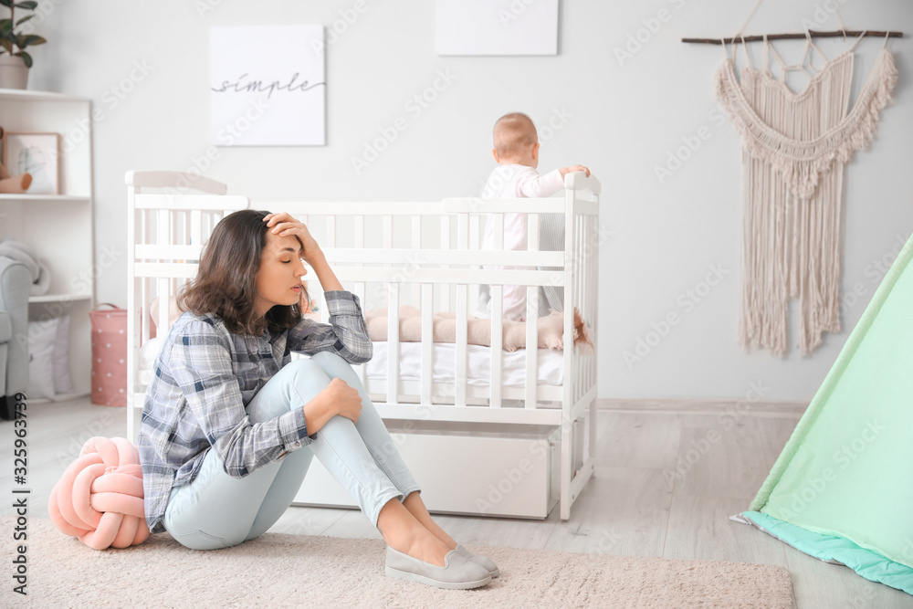 Young woman suffering from postnatal depression near bed with baby at home Young woman suffering from postnatal depression near bed with baby at home