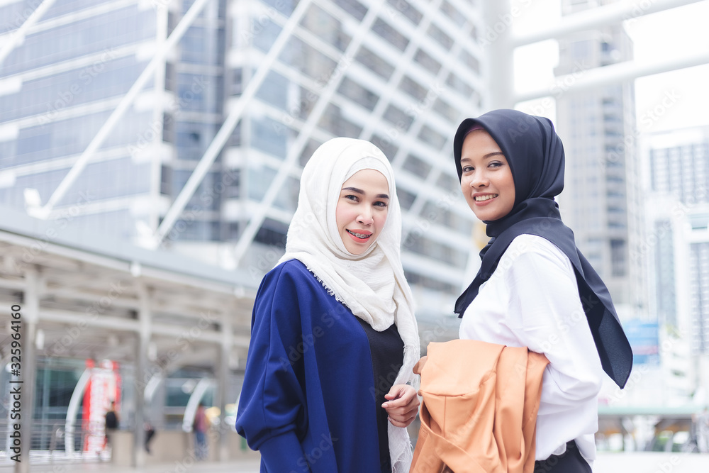 Two asian muslim woman standing and smiling looking camera in city.