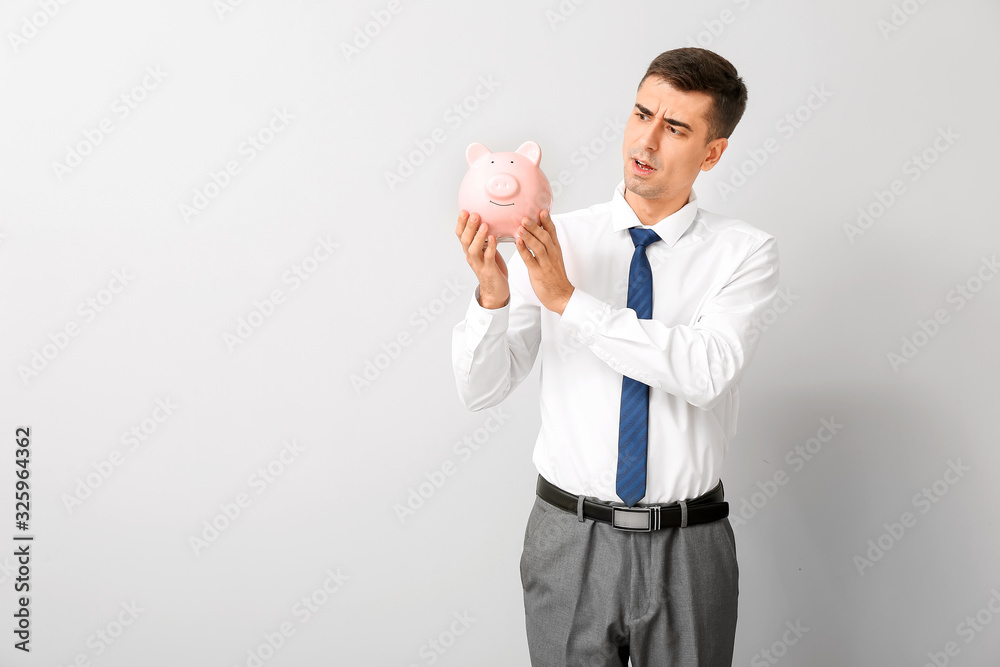 Worried businessman with piggy bank on light background Worried businessman with piggy bank on light background