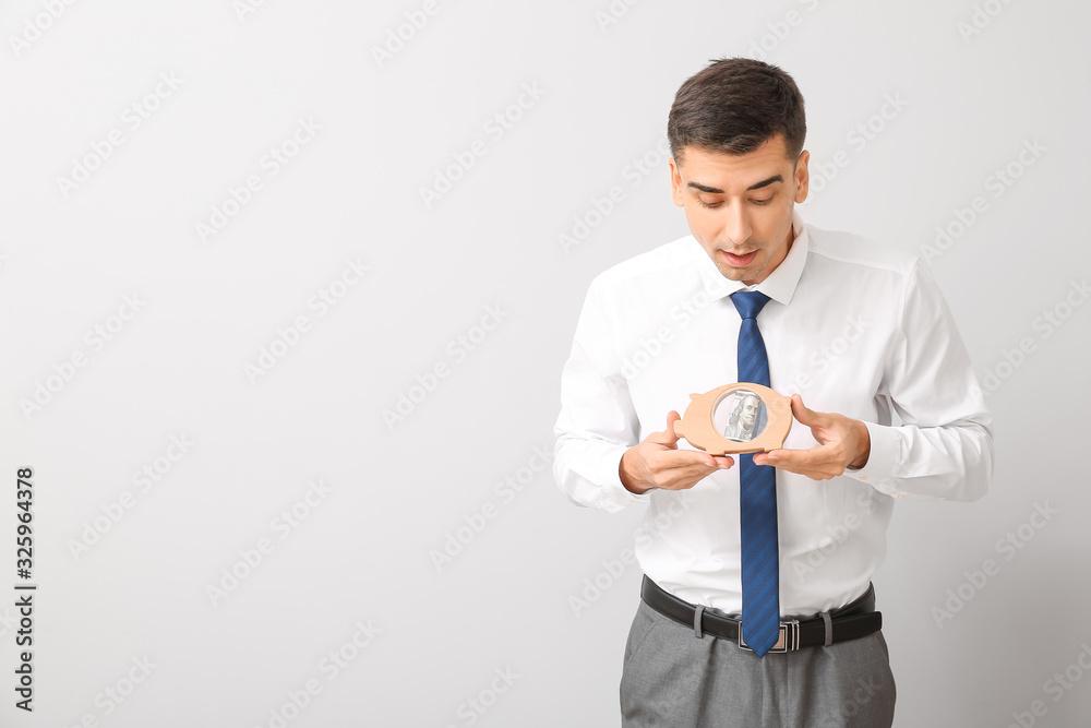 Surprised businessman with piggy bank on light background Surprised businessman with piggy bank on light background