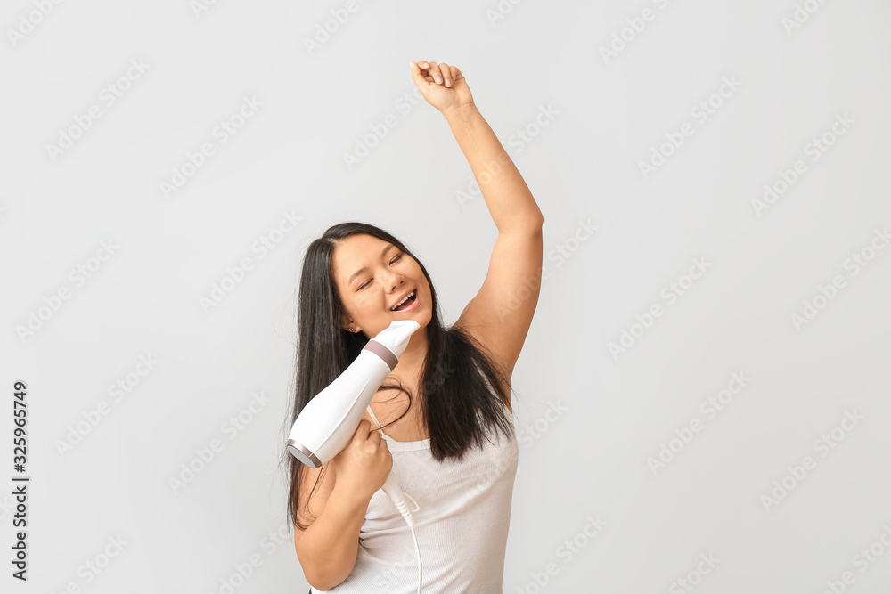 Beautiful Asian woman with hair dryer on light background Beautiful Asian woman with hair dryer on light background
