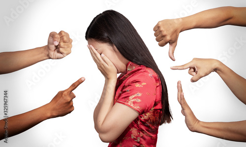 Asian woman in Chinese costume covered her face with regret for being racism and hate surrounded by hands mocking her, scoffing in the outbreak situation of Coronavirus 2019 infection or Covid-19 photo
