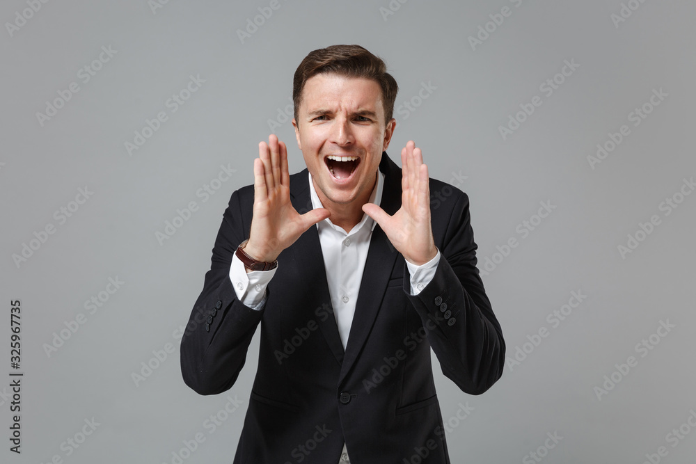 Young business man in classic black suit shirt posing isolated on grey background in studio. Achievement career wealth business concept. Mock up copy space. Screaming with hands gesture near mouth. Young business man in classic black suit shirt posing isolated on grey background in studio. Achievement career wealth business concept. Mock up copy space. Screaming with hands gesture near mouth.