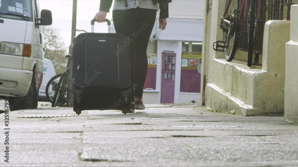 Woman pulling black  suitcase down the street.