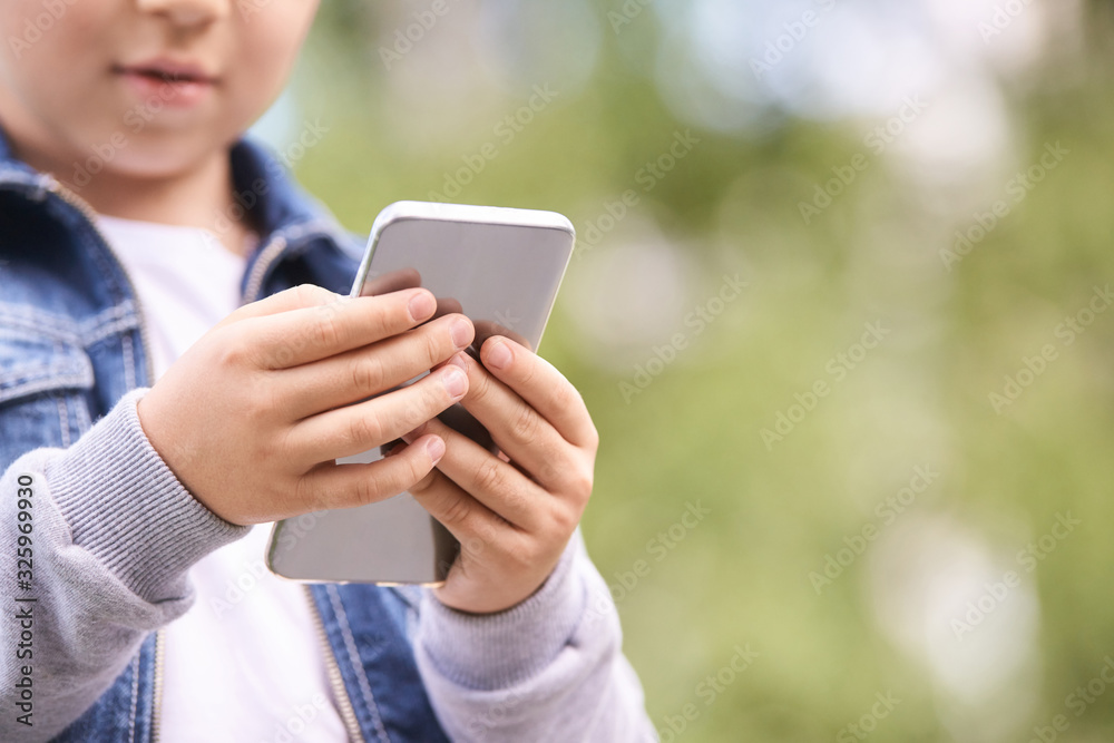 Young school boy texting outdoor. Male person using smartphone. Little hands with cell phone. Green bokeh street background. Young school boy texting outdoor. Male person using smartphone. Little hands with cell phone. Green bokeh street background.
