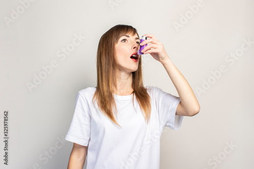 young woman holds an inhaler in her hand and sprays on a light background. Banner. Concept for easier breathing, treatment of asthma, pharynx, larynx, trachea