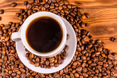 Cup of hot coffee and scattered coffee beans on wooden table. Top view