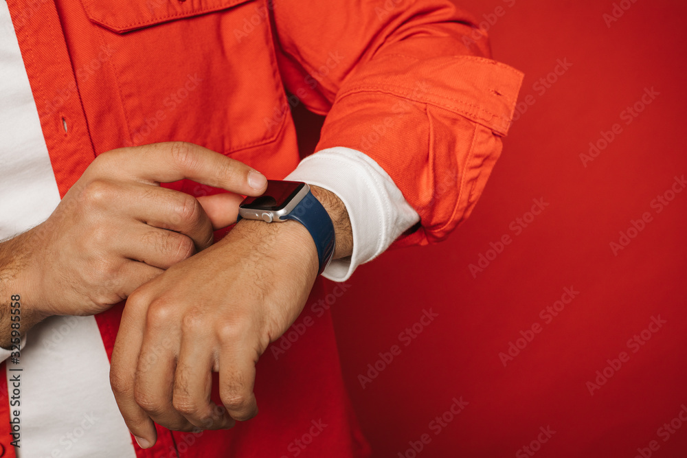 Close up and cut view of man's hands. Hispanic or arabian guy point on black watches. Smart gadget and modern technologies. Point with finger. Isolated over red background.