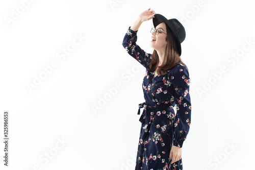 A brunette in a long floral dress with a hat poses for the camera in the studio. Emotional portrait © makedonski2015