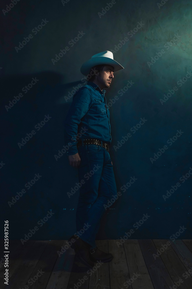 Man wearing denim shirt and cowboy hat standing against wall. Man wearing denim shirt and cowboy hat standing against wall.