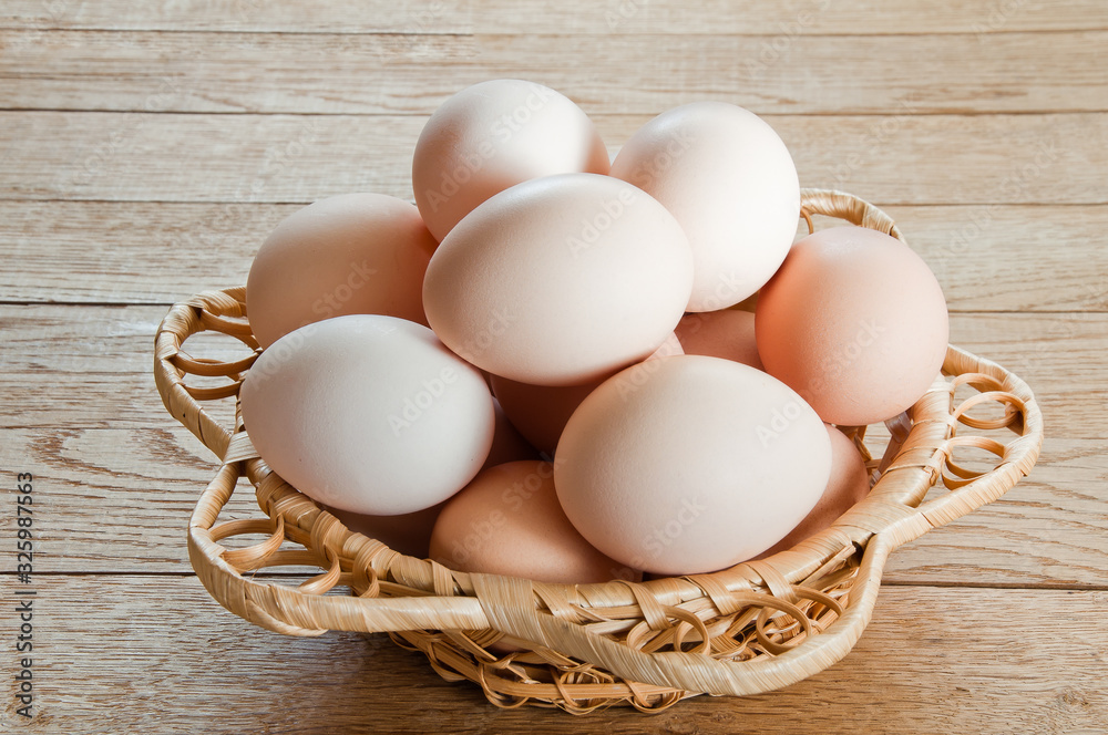 Fresh chicken eggs in wicker basket on wooden table