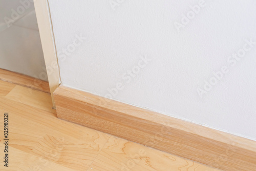 Wooden wall base skirting  finishing material with wood laminate floor and white mortar wall. Empty room with white wall and wooden floor.