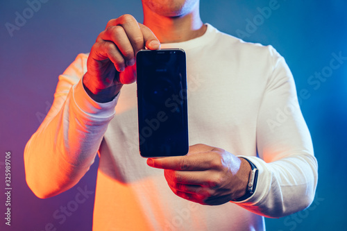 Cut view of young arabian man hold black smartphone with both hands. Show it on camera. Modern techologies in advertisement. Technologies. Isolated over colorful background. photo