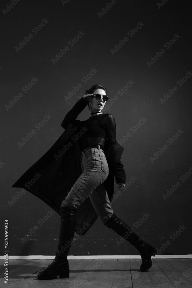 Black and white fashion shot. Portrait of a fashionable girl in high boots, a long coat, jeans and sunglasses. 