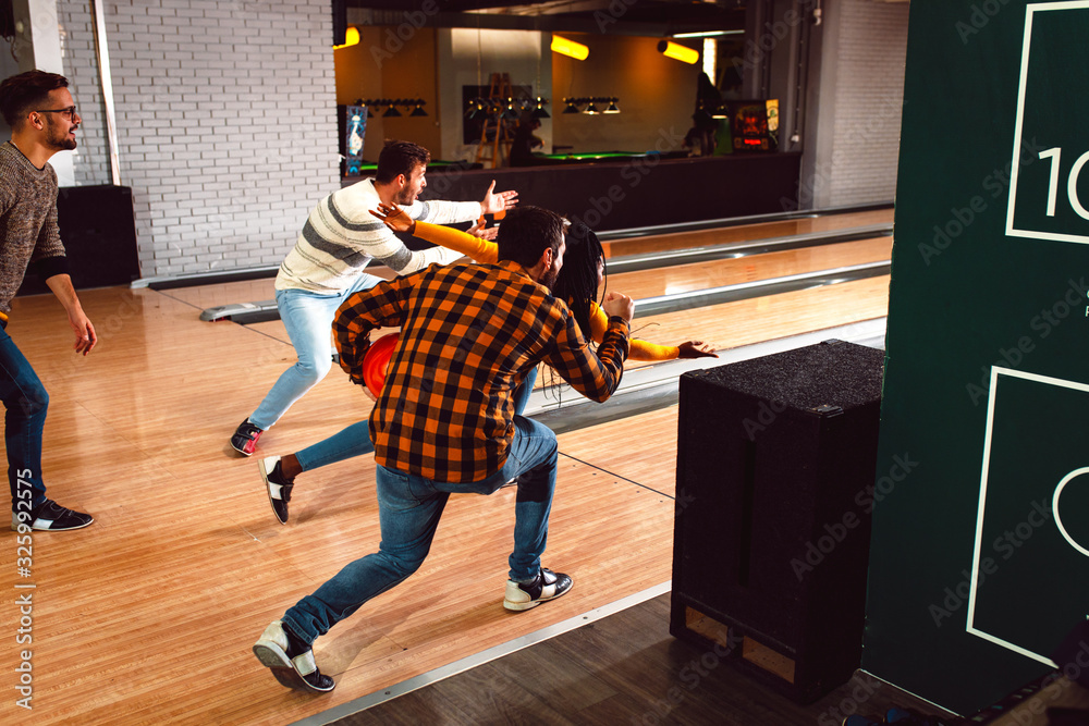 Obraz premium Group of friends enjoying time together laughing and cheering while bowling at club.