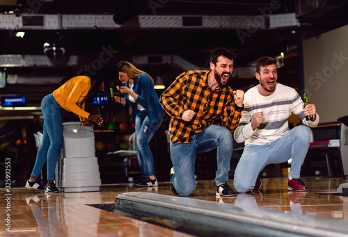 Group of friends enjoying time together laughing and cheering while bowling at club.
