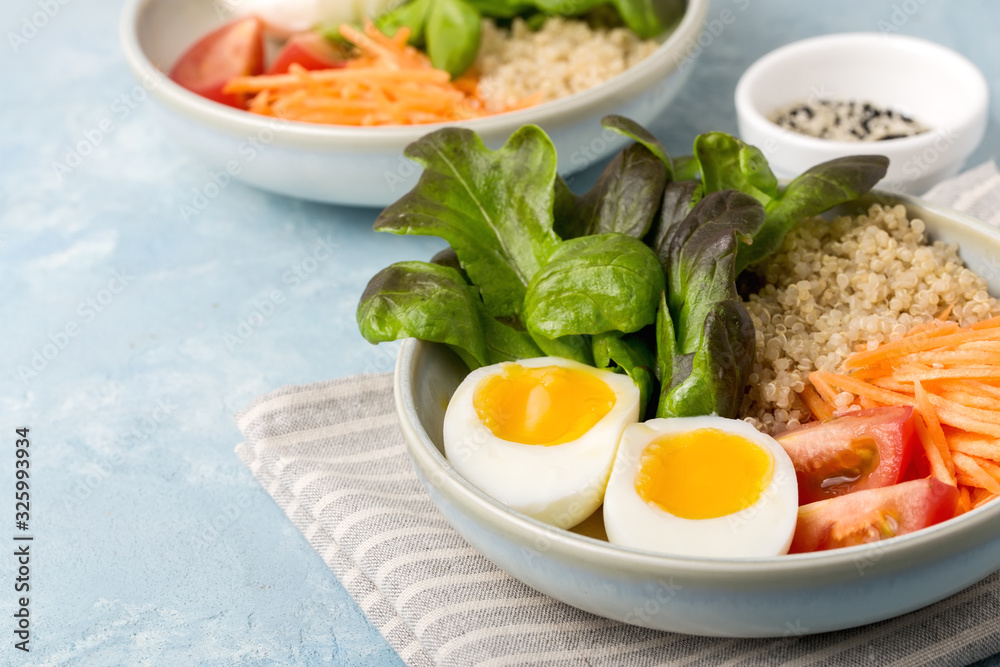 Healthy green vegetarian buddha bowl lunch with eggs, quinoa, carrots,tomato, lettuce leaves, on a blue background. Healthy green vegetarian buddha bowl lunch with eggs, quinoa, carrots,tomato, lettuce leaves, on a blue background.