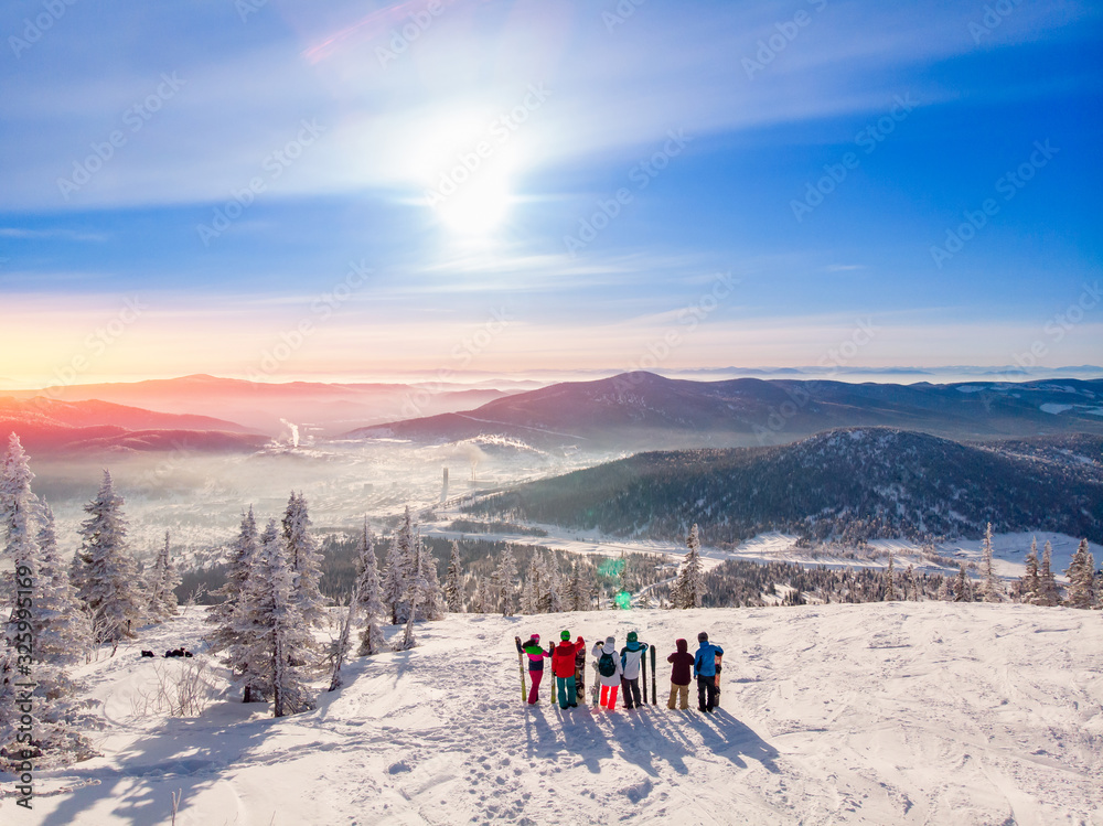 Six friends of skiers and snowboarders are standing on mountain in background of ski resort. Aerial top view
