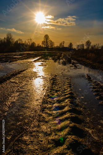Flooded dirty rural road in a mysterious backlight from the sun giving lens flare