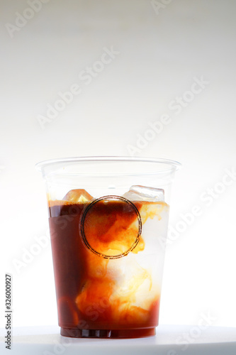 Iced coffee takeaway cup with liquid pouring down into container isolated on white background