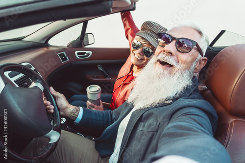 Happy senior couple taking selfie on new convertible car - Mature people having fun together during road trip vacation - Elderly lifestyle and travel transportation concept