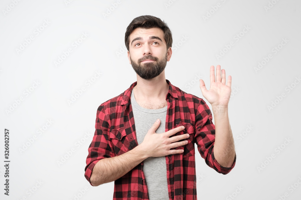 Sincere hispanic male with beard raising palm and holding hand on chest Sincere hispanic male with beard raising palm and holding hand on chest