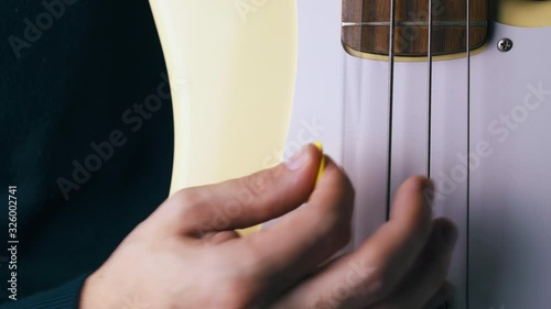 CU: professional music teacher plays vertical guitar with metal bass stripes holding yellow pick close view photo