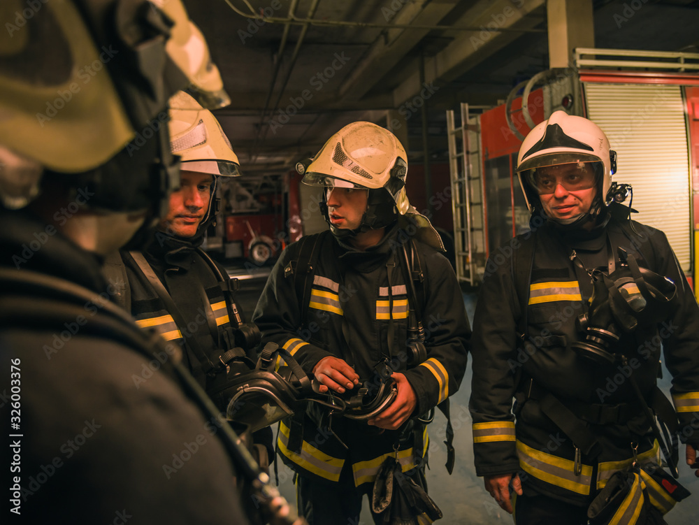 Group of firefighters with uniform inside the fire station preparing for safe rescue Group of firefighters with uniform inside the fire station preparing for safe rescue