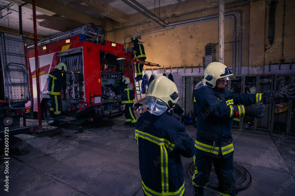 Firefighters preparing their uniform and the firetruck in the background inside the fire station Firefighters preparing their uniform and the firetruck in the background inside the fire station