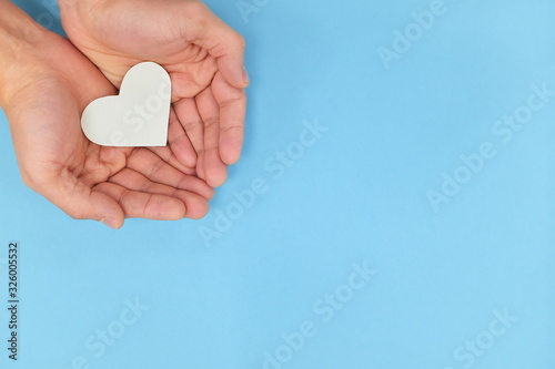 Hands holding a white heart in blue background. Charity, pure love and kindness concept. Top view photo