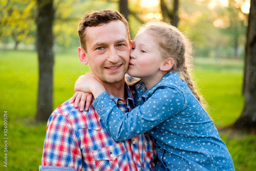 Fototapeta premium Daughter kissing young happy father in summer park on natural green background. Happy loving family concept