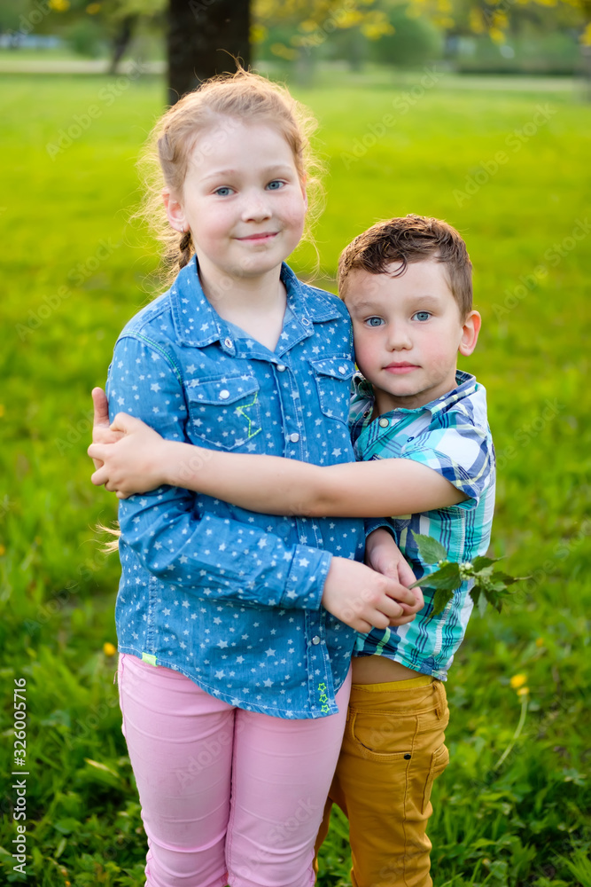 Cute little boy hugs him sister girl on green grass in park, cheerful